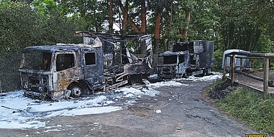 Zwei ausgebrannte Lkw mit Löschschaum auf einer Straße