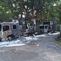 Zwei ausgebrannte Lkw mit Löschschaum auf einer Straße